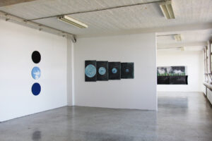 Exhibition view showing three vertically arranged circular paintings and a four-panel work on the wall